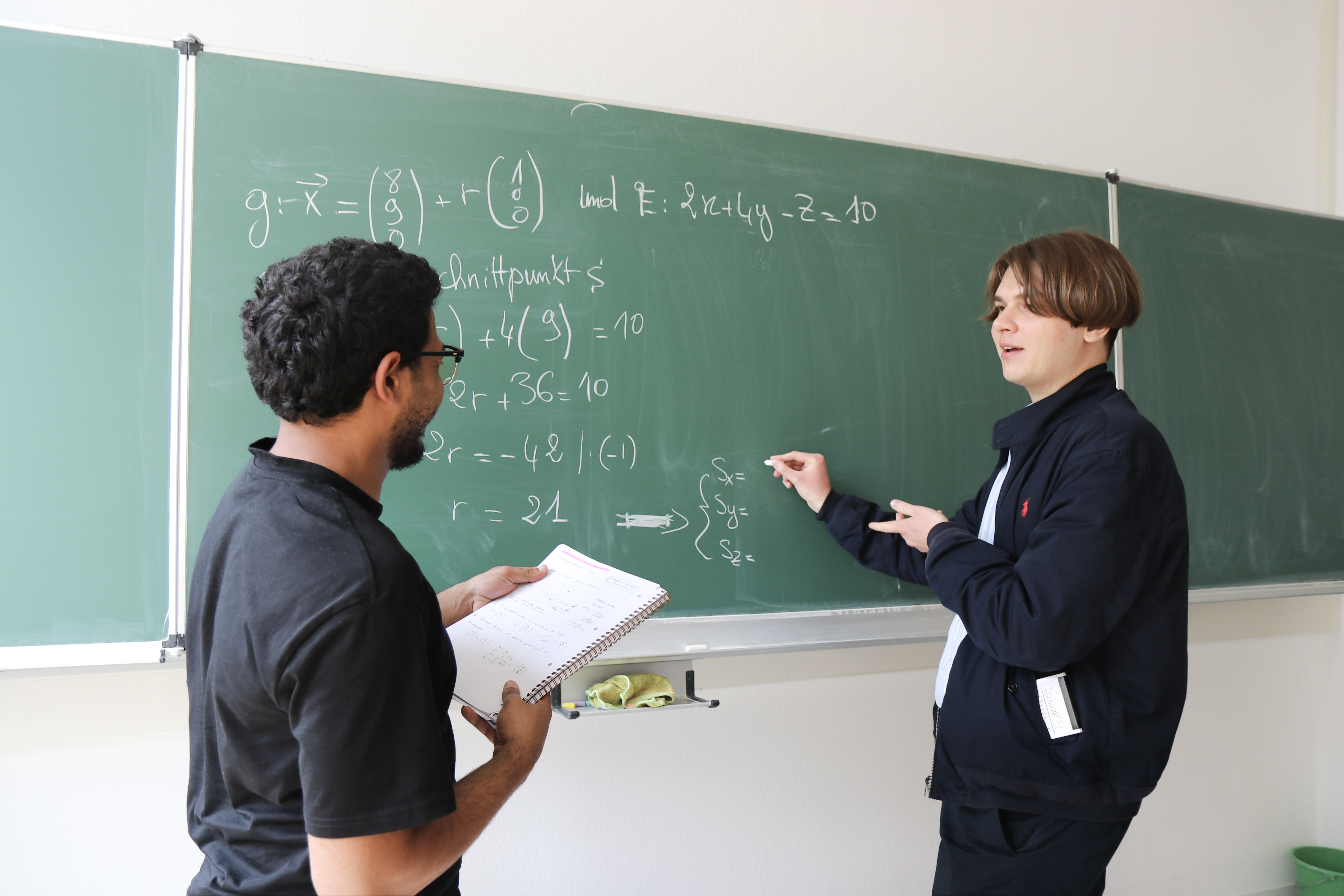 Ein Lehrer erklärt mathematische Konzepte, während ein Student an einer Tafel steht.