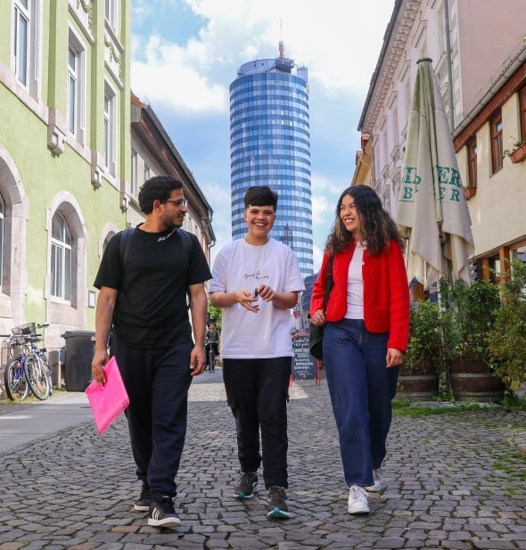 3 junge Menschen erkunden eine malerische Straße in Jena mit historischen Gebäuden.