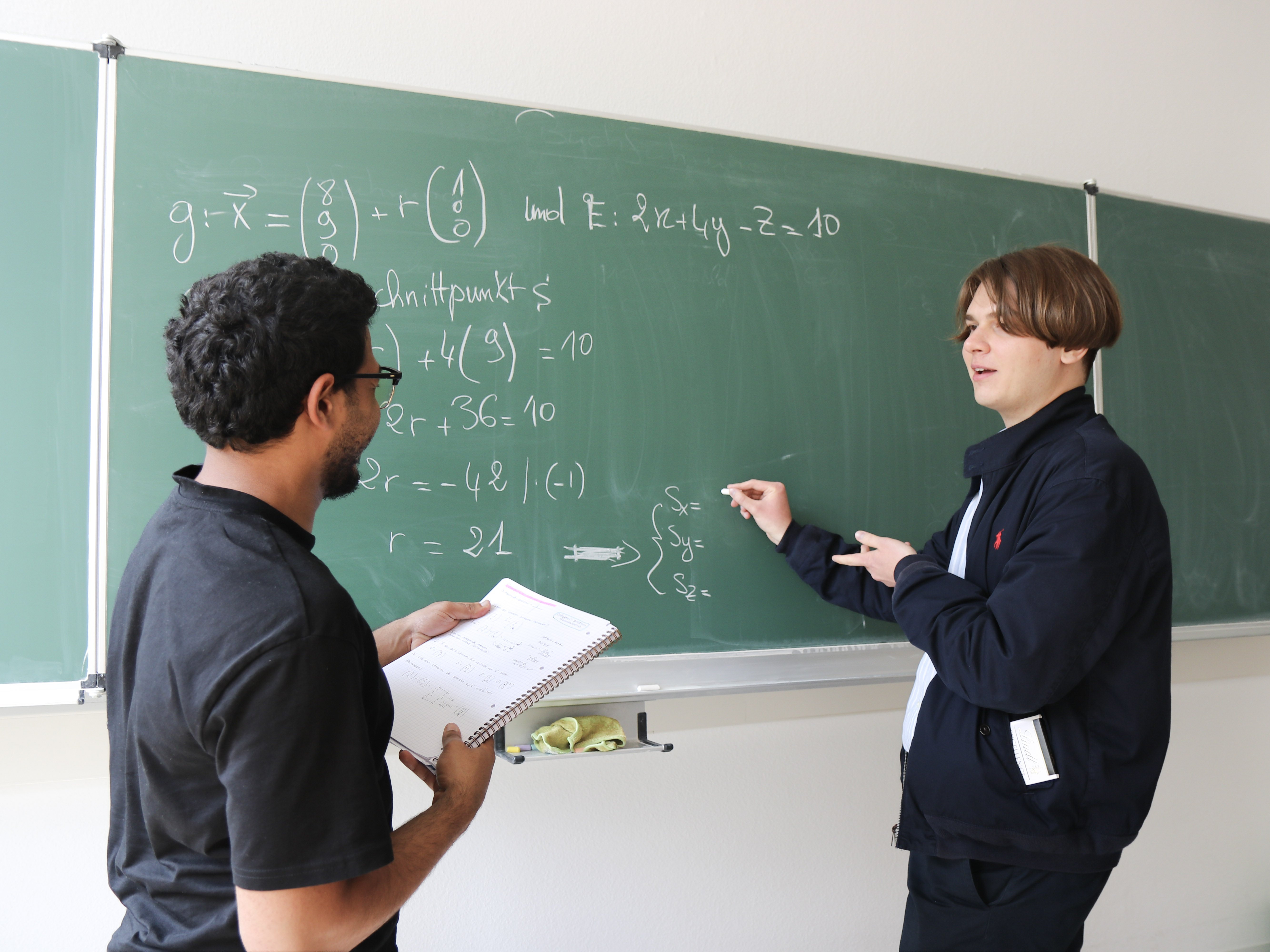 Schüler diskutieren Mathematik an einer Tafel in einem Klassenzimmer.